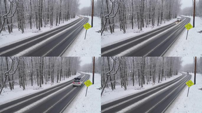 皮卡车和其他汽车在降雪下驾驶高速公路穿过森林。带有静态摄像机的无人机航拍视频。