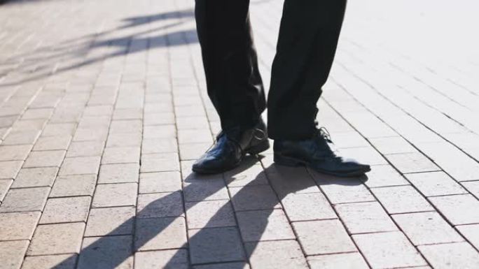 穿着黑色鞋子和裤子的男性的脚在户外的人行道上快乐地跳舞。