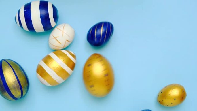 复活节彩蛋在滚动，互相敲在蓝色的桌子上。鸡蛋时尚彩色经典蓝色、白色和金色。复活节快乐。最小风格。顶视