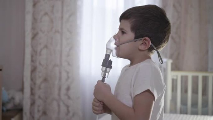 生病的儿童在家中通过吸入器面罩吸入，通过雾化器治疗气道炎症，以防止哮喘和咳嗽坐在床上