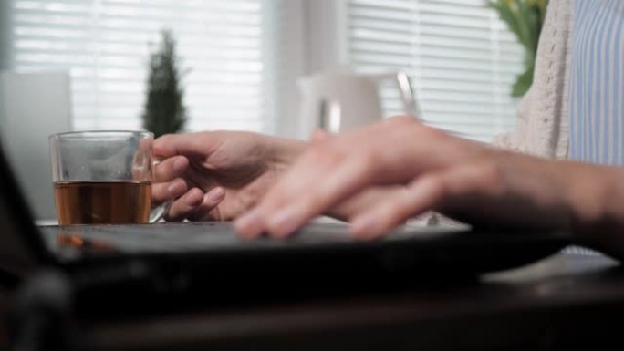 女性双手在笔记本电脑键盘上打字，打断右手举起茶杯，放下茶杯，工作恢复。社交网络，通信，自由职业者，学