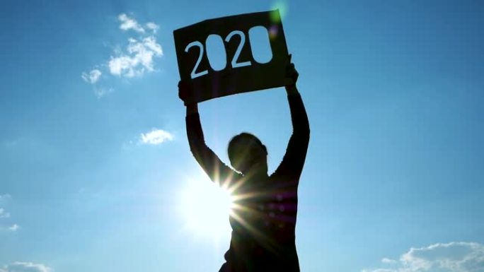 女人的剪影拿着回收纸板，2020文本在日落天空背景和阳光透过文本。新年和庆祝活动的概念。