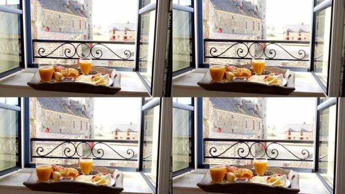 窗台上放着法式早餐的托盘。羊角面包，奶酪，果汁，果酱，樱桃番茄和法式长棍面包