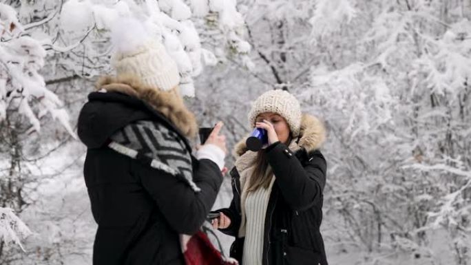 朋友们在森林里享受冬日，用绝缘饮料容器喝茶，说话和微笑