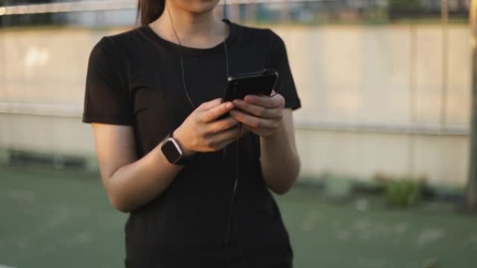 美丽的年轻亚洲女子慢跑在温暖的晴天使用智能手机在秋天听音乐。