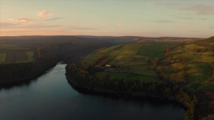 日落时分，航拍画面飞越英国约克郡和德比郡谢菲尔德的布拉德菲尔德村，峰区国家公园，平静的阿格登湖水库。