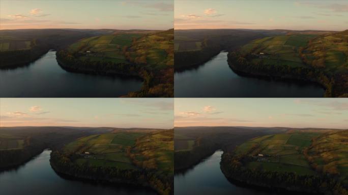 日落时分，航拍画面飞越英国约克郡和德比郡谢菲尔德的布拉德菲尔德村，峰区国家公园，平静的阿格登湖水库。