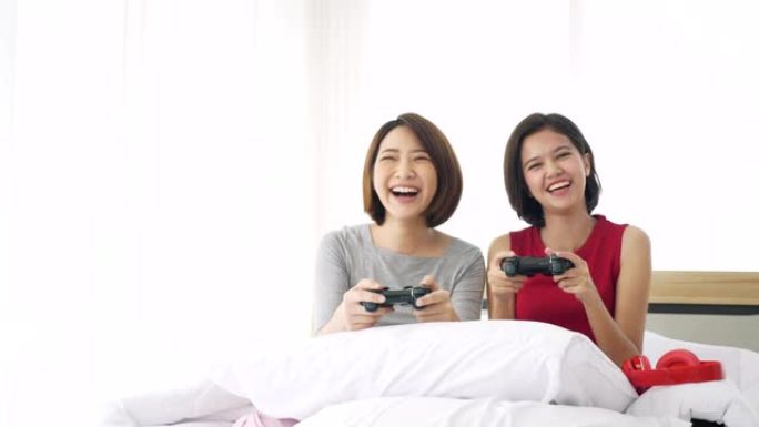两个亚洲女人坐在床上，一起玩游戏的操纵杆。