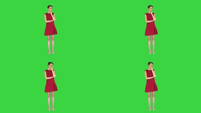 穿着红色连衣裙的迷人年轻女子站在绿色屏幕上听某人说话，色键