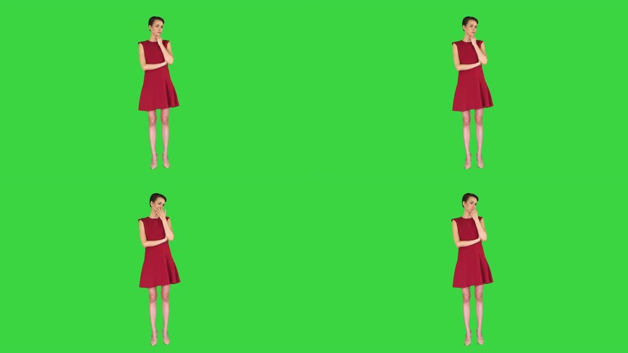 穿着红色连衣裙的迷人年轻女子站在绿色屏幕上听某人说话，色键