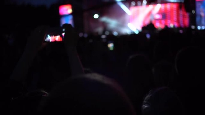 晚上的音乐会，人们举手，用智能手机拍照，