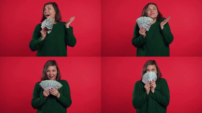 快乐兴奋的女孩穿着绿色毛衣显示钱-红墙上的美元钞票。成功、收获、胜利的象征。