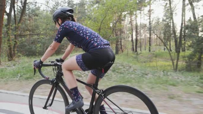 年轻的女自行车手在公园骑自行车，这是她训练的一部分。侧面跟随射击。慢动作