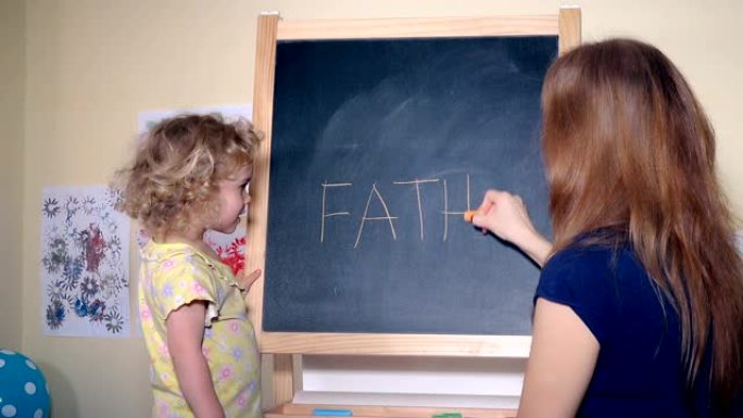 幸福的家庭女孩妈妈和女儿在黑色粉笔板上写单词父亲