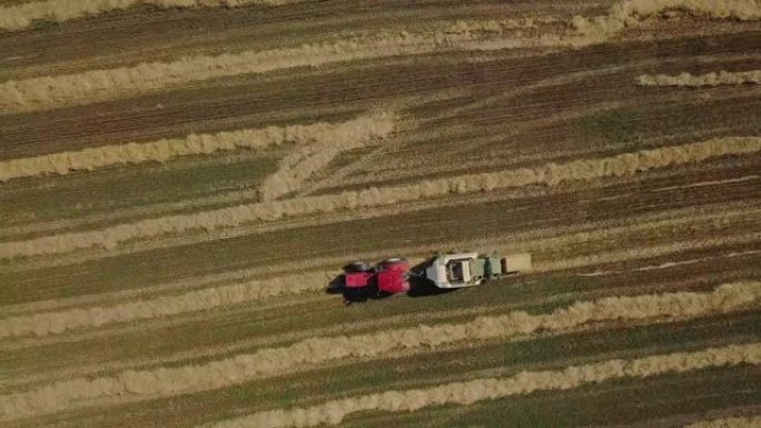 用拖拉机制作干草立方体的无人机镜头。农业机械在阳光明媚的日子里喷出干草。干草堆在田野里。