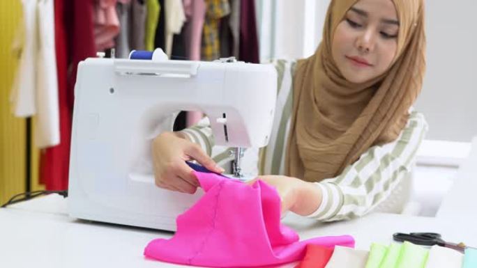穆斯林女性时装设计师在家庭工作室的电动缝纫机上纺织，倾斜镜头