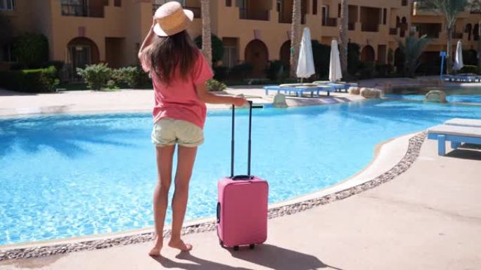 穿着粉红色箱子的年轻女子住在酒店游泳池附近。旅游度假概念。1920x1080中的高清视频