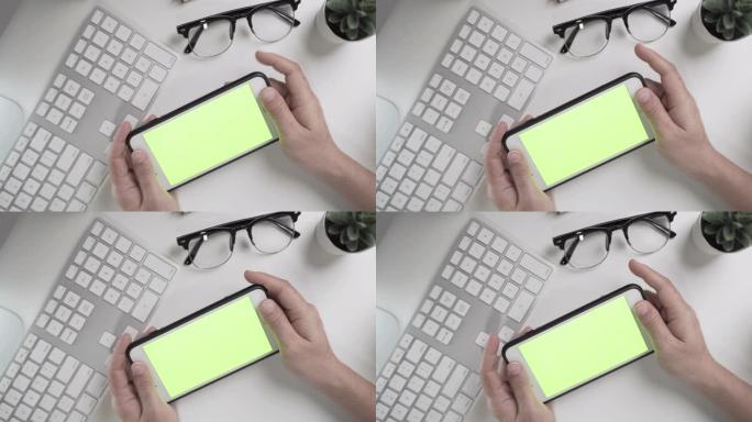 办公桌和女商人的手的特写镜头显示了智能手机上的绿色屏幕。顶视图