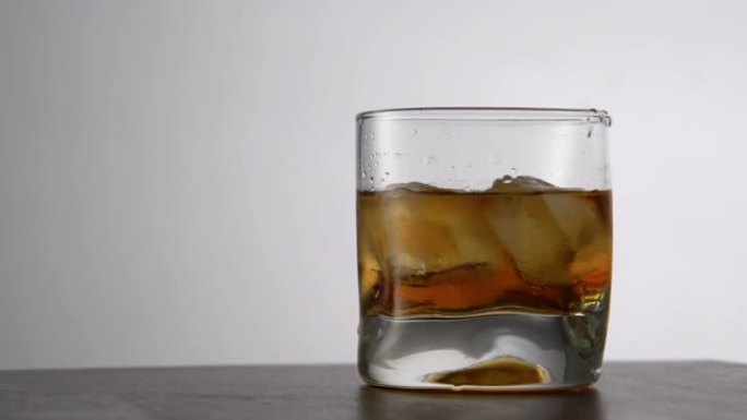 一杯陈年的金威士忌和冰块放在桌子上。酒吧里有石头的琥珀色酒精饮料