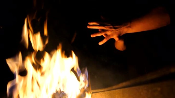 晚上，年轻游客的低视野在曼加尔 (mangal) 的篝火前擦手。男人在黑色背景下用金属火盆的火加热手