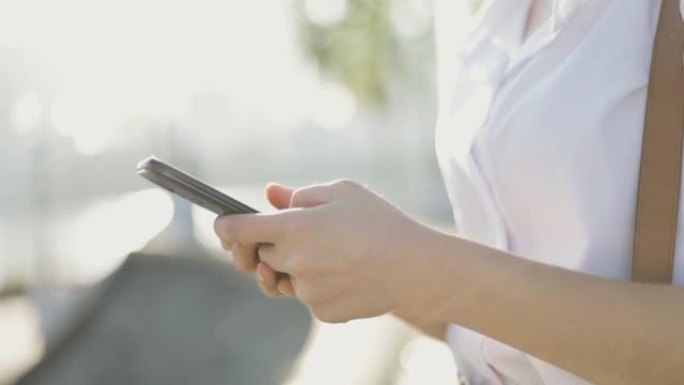 身穿白衬衫的亚洲女商人正在使用智能手机在公园外的社交媒体上发短信分享消息。