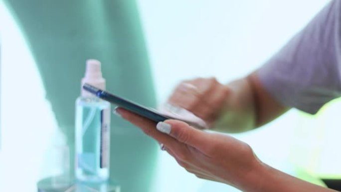 女性使用酒精喷雾和擦拭智能手机表面清洁和保护新型冠状病毒肺炎