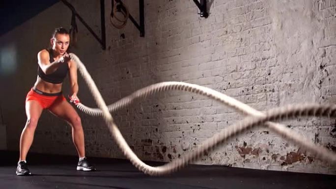 迷人的年轻健康的女运动员在功能训练馆做运动与战斗绳