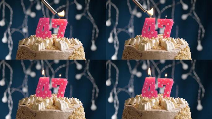 蓝色背景上有47号粉色蜡烛的生日蛋糕。蜡烛着火了。慢动作和特写视图