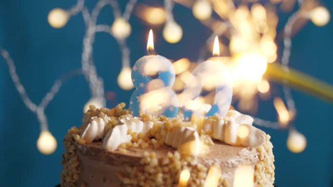 蓝色背景上有80号蜡烛和烟火的生日蛋糕。慢动作和特写视图