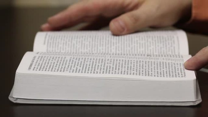 桌子上有一本开放的圣经。一个人慢慢地翻阅页面寻找所需的章节。特写镜头。