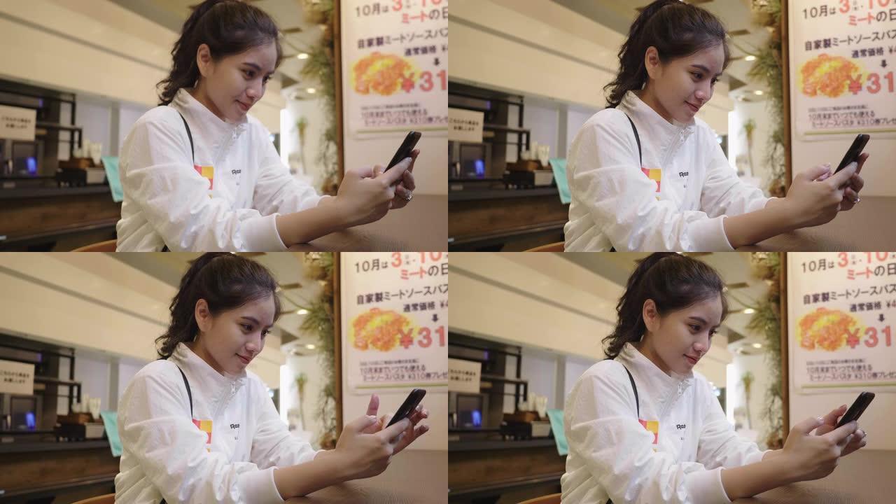 年轻的亚洲妇女在餐厅检查智能手机