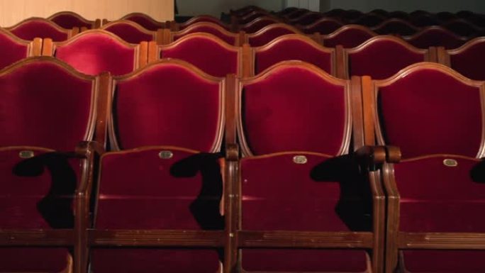 剧院座位排成一行，由空荡荡的剧院大厅中的聚光灯红色天鹅绒椅子照亮