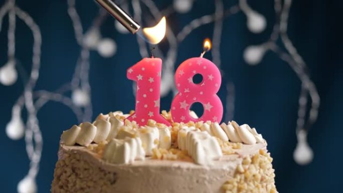 蓝色背景上有18号粉色蜡烛的生日蛋糕。蜡烛着火了。慢动作和特写视图