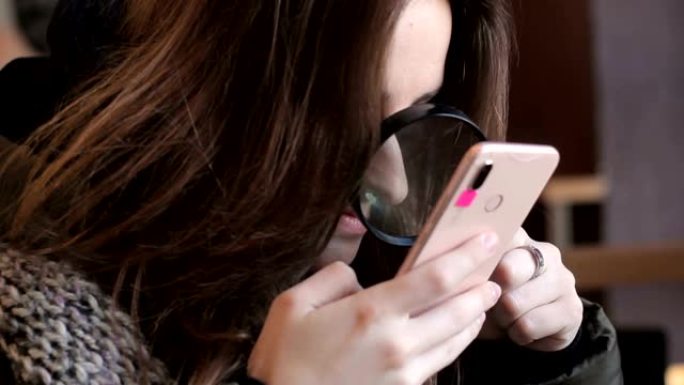 棕色头发的女孩看着屏幕智能手机放大镜气体。