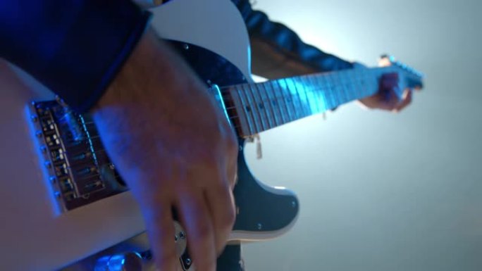 摇滚音乐家mans hands熟练演奏电吉他的特写镜头。在舞台上的音乐会上，手指在烟熏的聚光灯下敲击