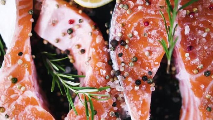 迷迭香小枝滴在喜马拉雅盐生鲑鱼牛排上，辣椒和柠檬的混合物，俯视图，旋转，慢动作。健康食品的概念。