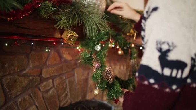 穿着针织衫的人在石头正宗壁炉上方悬挂圣诞花环，装饰着五颜六色的闪光花环灯。新年假期准备和装饰。近距离