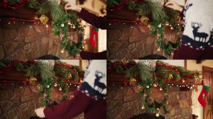 穿着针织衫的人在石头正宗壁炉上方悬挂圣诞花环，装饰着五颜六色的闪光花环灯。新年假期准备和装饰。近距离