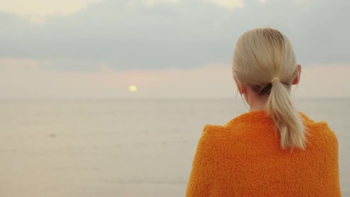 独自在海上迎接日出。一个裹着毯子的女人看起来像太阳在海上升起