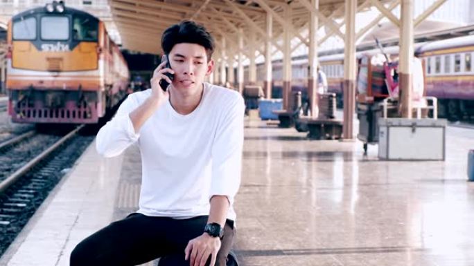 在曼谷火车站等火车的嬉皮士，打电话，背景是火车。亚洲人。
