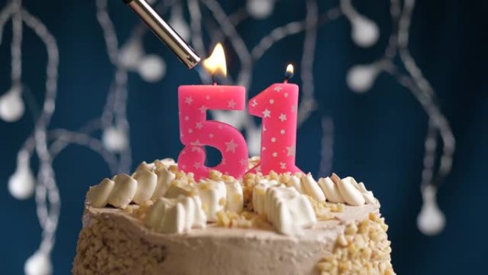 蓝色背景上有51号粉色蜡烛的生日蛋糕。蜡烛着火了。慢动作和特写视图