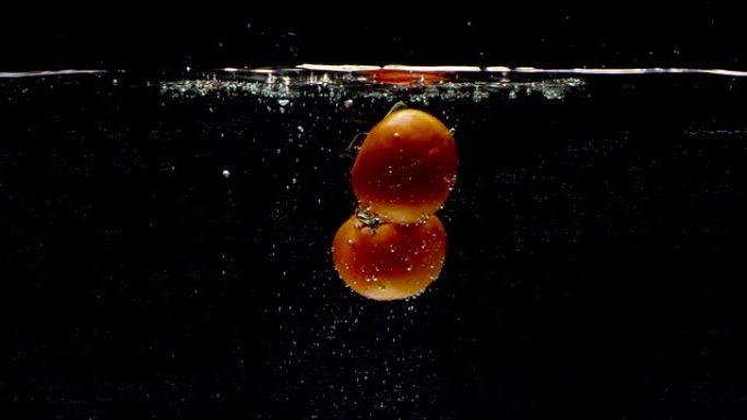 西红柿以慢动作落入水中。孤立在黑色背景上。特写视图。用电影相机拍摄红龙，FHD，240fps