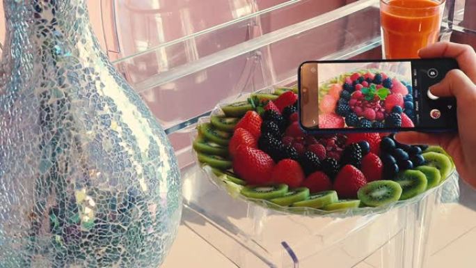 女人在智能手机上拍摄水果盘子的照片