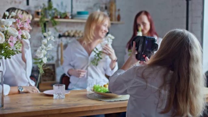 女摄影师用年轻迷人女性的专业相机拍照。女人摆着鲜花，微笑着。舒适照相馆的照相馆。
