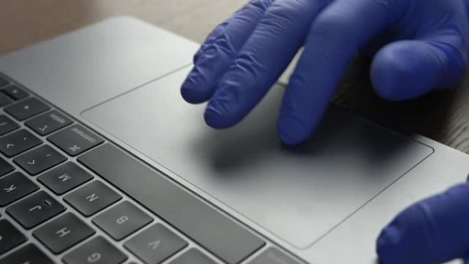 医生的手在办公室笔记本电脑上使用触控板触摸板戴蓝色手术手套