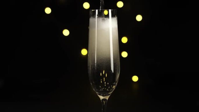 将香槟或起泡酒倒入玻璃中，以黑色背景为黑色。上面冒出气泡和白色泡沫。特写