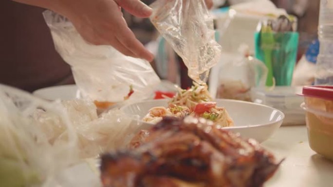 亚洲高级妇女从塑料袋中拿出泰国食物准备在桌子上吃。在家外卖。