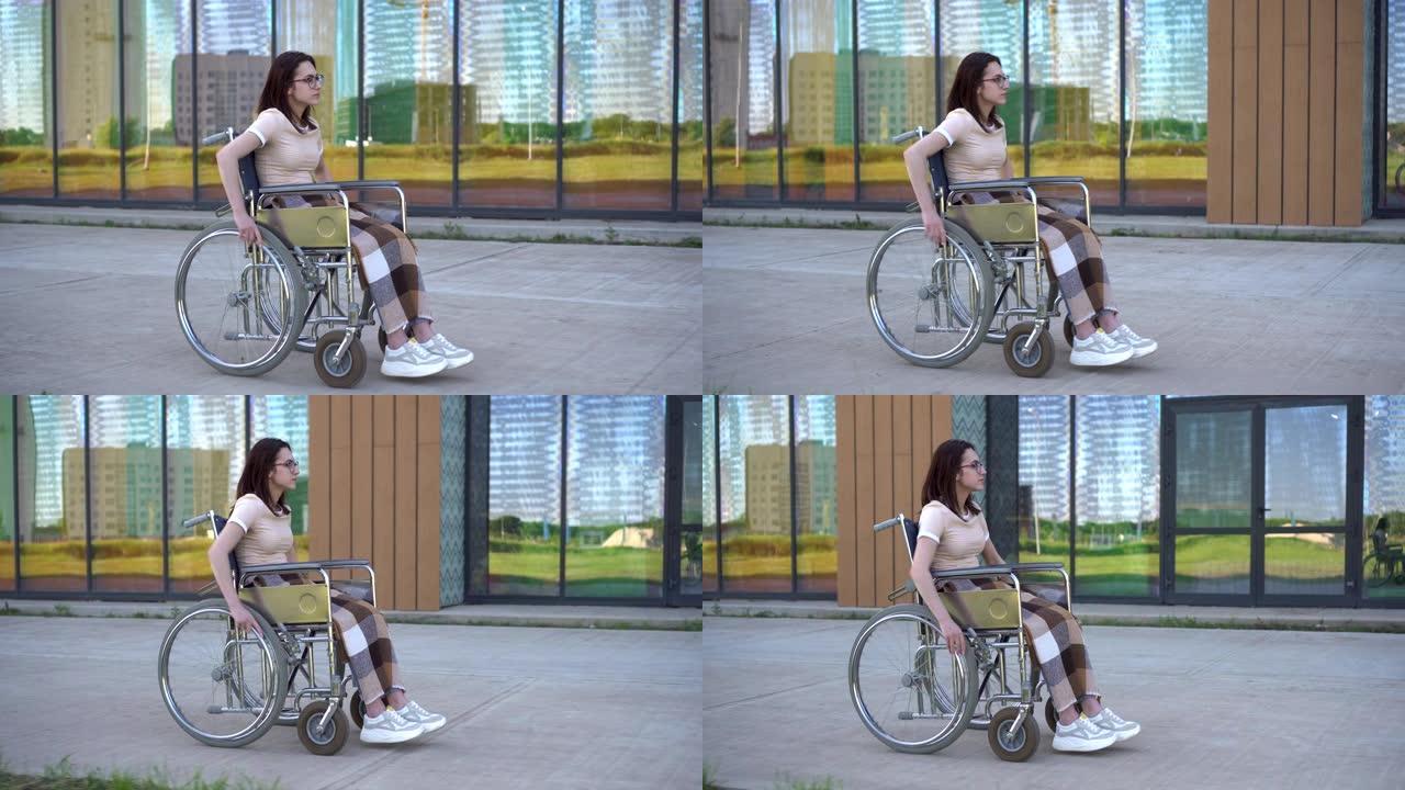 坐在轮椅上的年轻女子。一个女孩在玻璃建筑的背景下坐在轮椅上。残疾人专用交通工具。