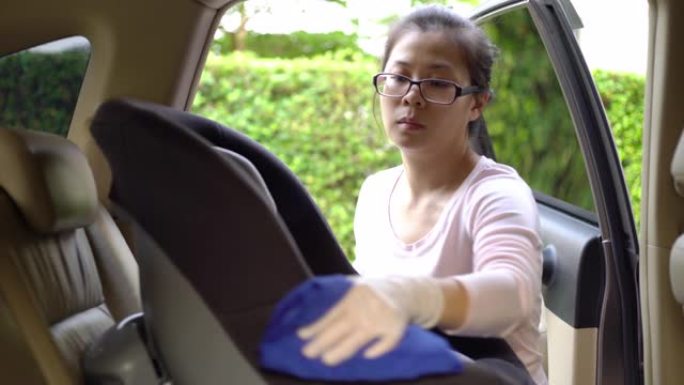 使用酒精喷雾和擦拭汽车安全座椅表面的带安全眼镜和手持手套的亚洲妈妈。