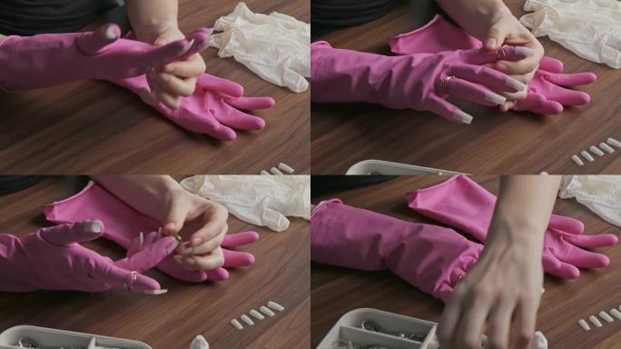年轻女子在手指上戴上金戒指。女性双手戴着粉红色的橡胶手套，戴着假指甲。安全和美丽的概念。特写。